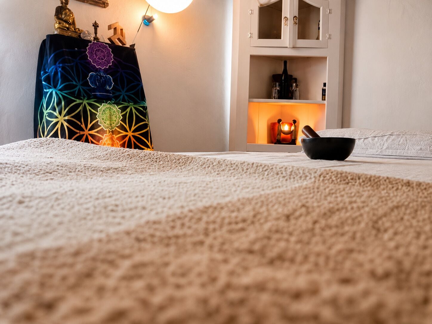 Un dormitorio con una cama, un adorno en la pared, un mueble con una vela encendida y un cuenco sobre la cama.