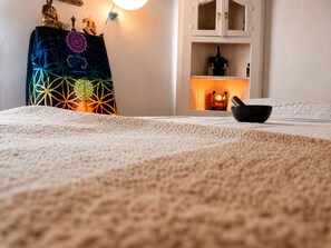 Une chambre à coucher avec un lit, une décoration murale, une armoire sur laquelle est posée une bougie allumée, et un bol sur le lit.