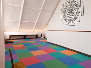Ein Zimmer mit schräg verlegtem Deckenbalken, bunte, ineinandergreifende Schaumstofffliesen, eine weiße Wand mit geometrischem Muster und eine Bank an der Wand.