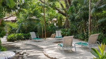 Un jardín con mobiliario exterior, un sendero y vegetación tropical.