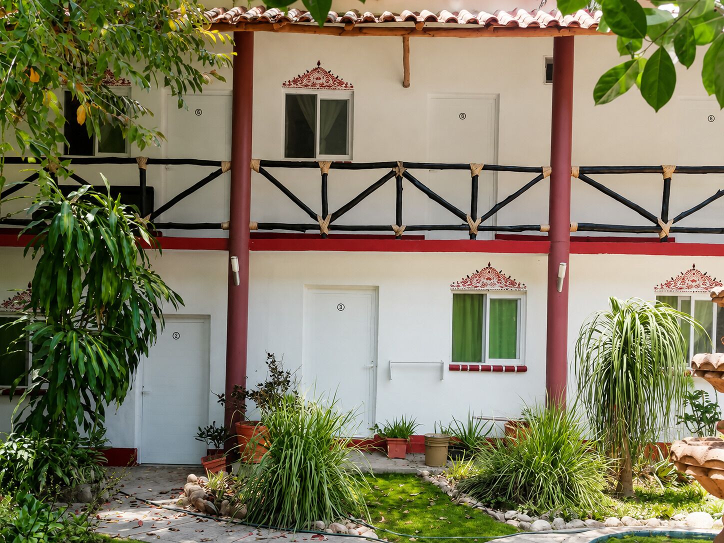 A two-story building with a balcony, potted plants, and a small garden area.