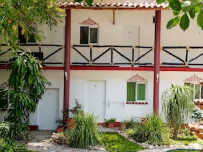 A two-story building with a balcony, potted plants, and a small garden area.