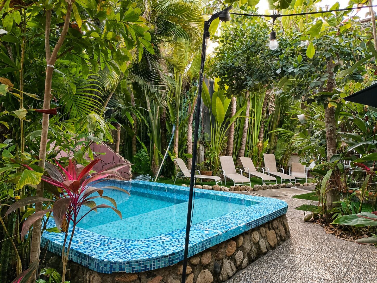 A pool area with a tiled edge, surrounded by lush greenery and lounge chairs.