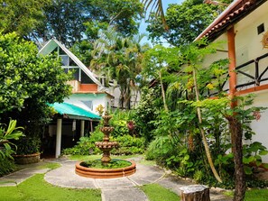 Un patio con una fuente, abundante vegetación y un edificio de techo de tejas.