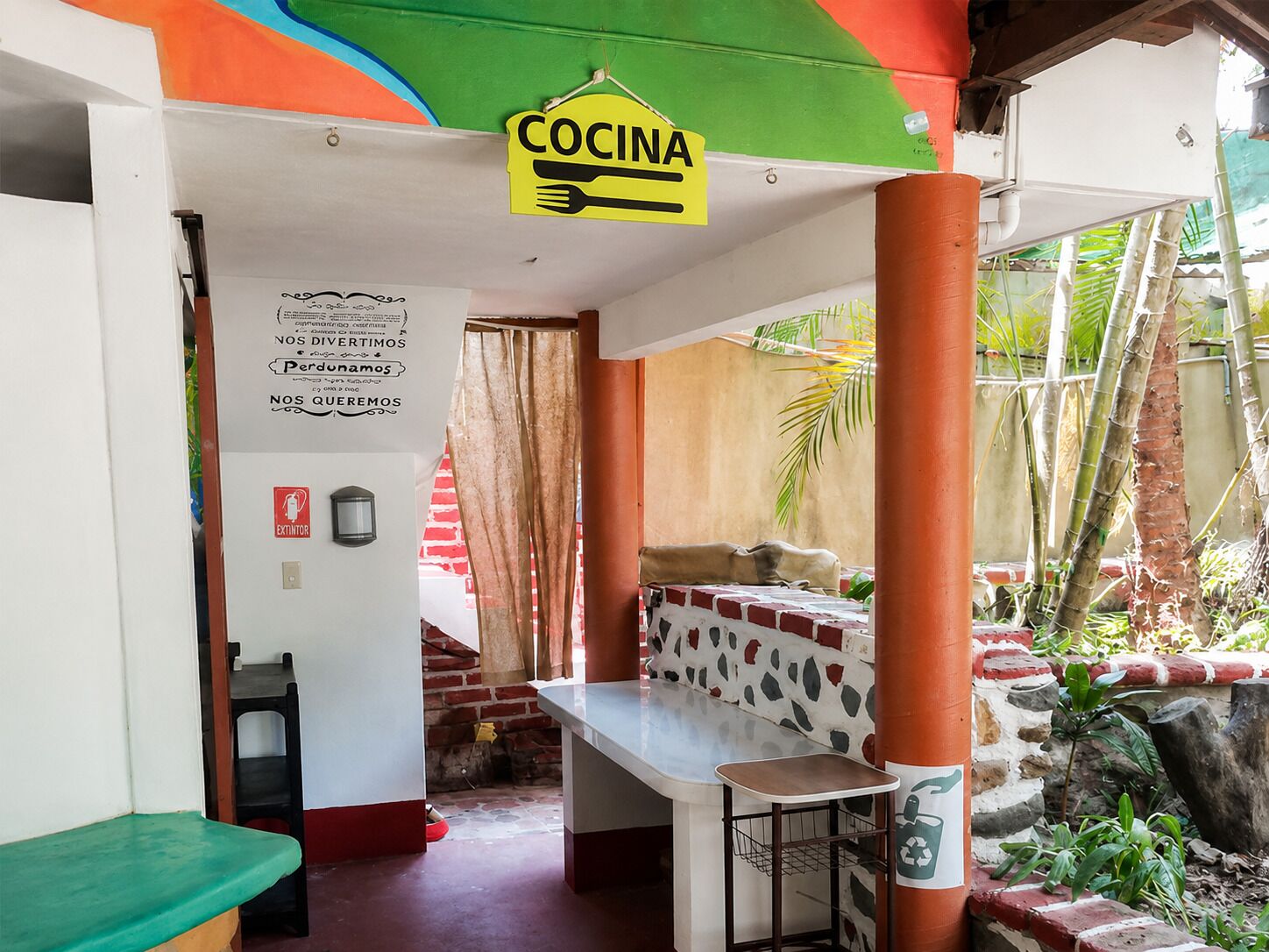 Ein Restaurant mit einem 'Cocina'-Schild, einer Ziegelwand, einem Tisch mit einem Korb und Blick auf Grünflächen draußen.