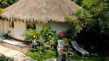 Una casa con techo de paja, un jardín, asientos exteriores y una fuente.