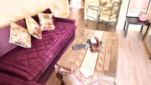 A living room with a purple sofa, a wooden coffee table with a decorative tray, and a glass table with chairs. - Apartment Sleeps 6 With in Kilburn Lane (London)