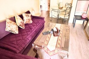Ein Wohnzimmer mit einem violetten Sofa, einem Couchtisch aus Holz mit einer Dekorationstasse und einem Glastisch mit Stühlen.