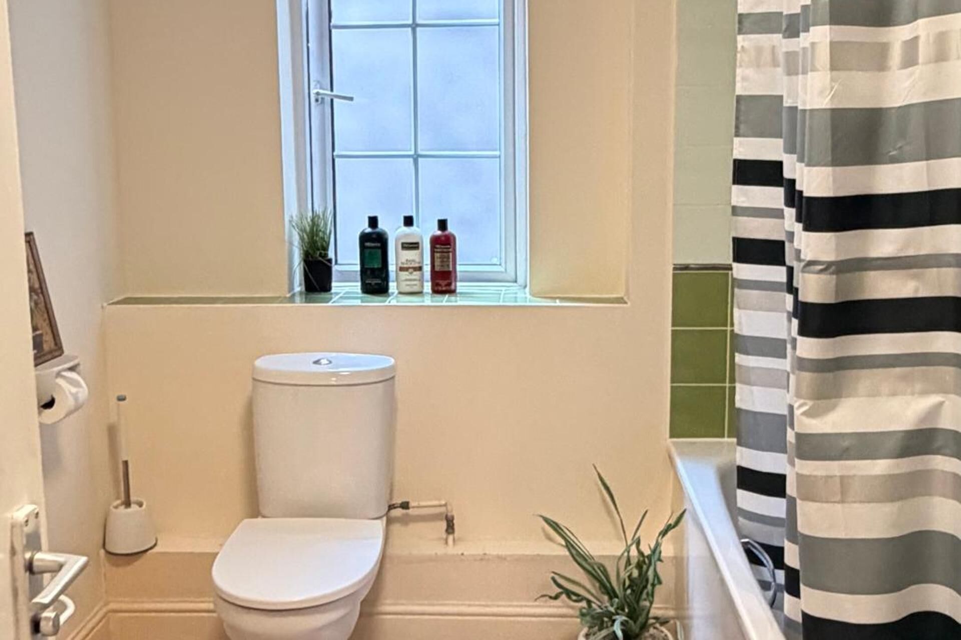 Une salle de bain avec des toilettes, une fenêtre où sont rangés les articles de toilette et un rideau de douche à rayures.