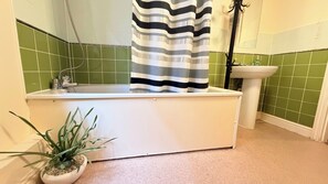 A bathroom with a bathtub, a sink, a shower, and a potted plant. - Apartment Sleeps 6 With in Kilburn Lane (London)