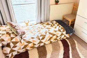 A bedroom with a bed, a chair, a radiator, and a window with blinds. - Apartment Sleeps 6 With in Kilburn Lane (London)