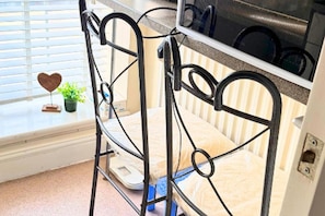 Ein Metallgestell-Stockbett mit integriertem Mikrowellenherd darüber, ein Fenster mit Jalousien und ein kleiner Blumentopf auf der Fensterbank.