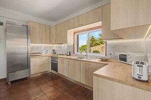 A modern kitchen with a stainless steel refrigerator, a dishwasher, a sink, a toaster, and a window with a view of greenery. - Villa Monte Galego. Private pool and garden. A space just for you. (Guia)