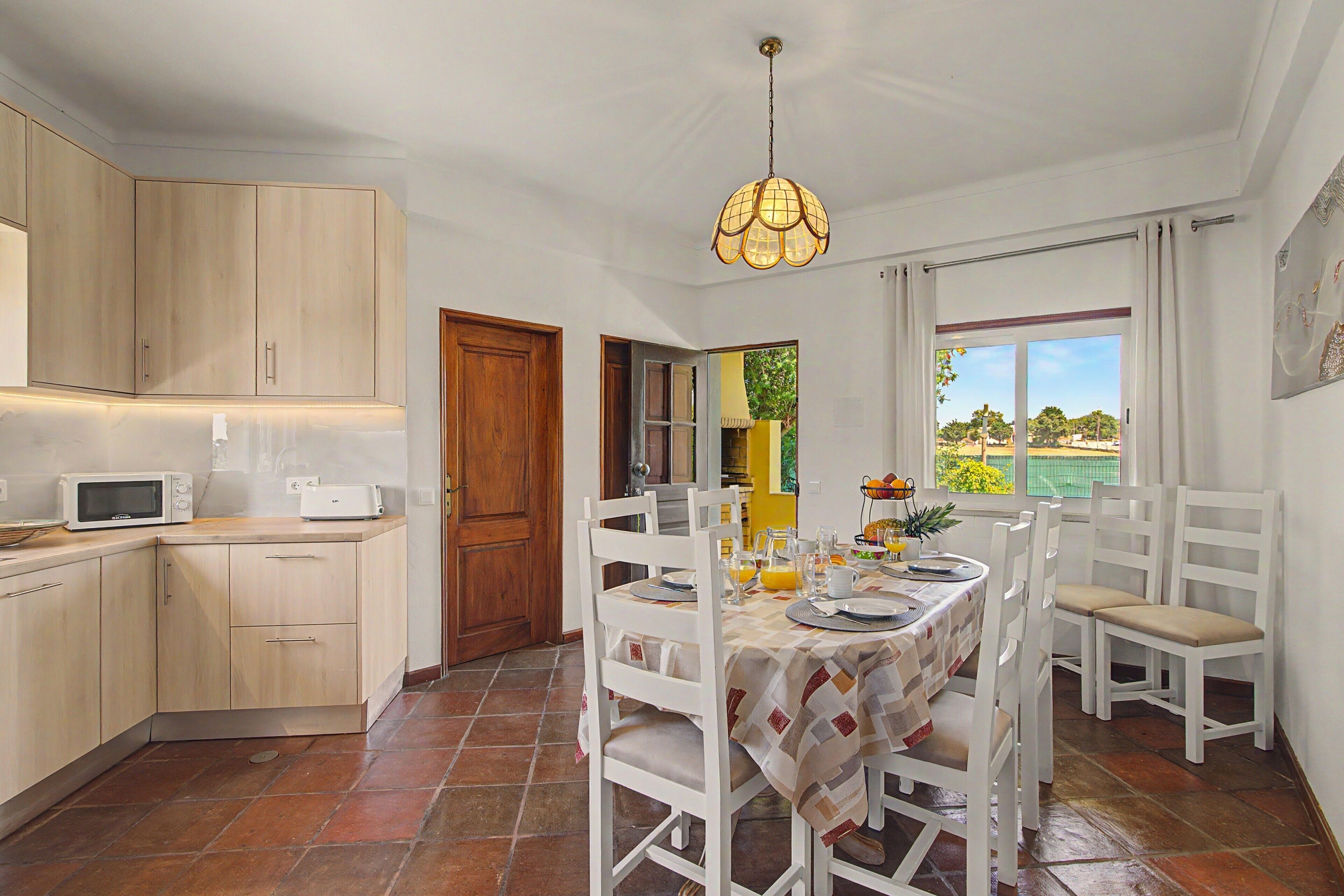 A kitchen with a microwave, cabinets, and a dining area with a table set for two.