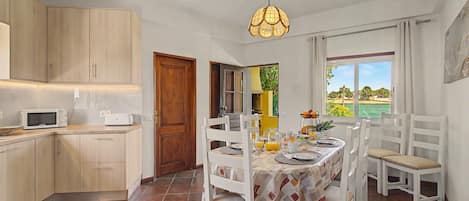 A kitchen with a microwave, cabinets, and a dining area with a table set for two.