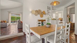 Un espace repas avec une table en bois et des chaises blanches, entouré de murs blancs ornés de décorations murales.