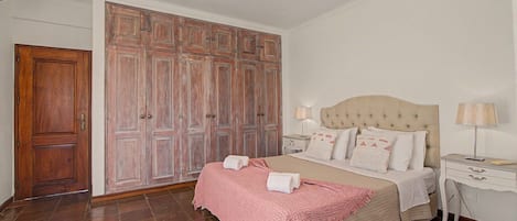 A bedroom with a bed, bedside tables, a wardrobe, and a tiled floor.