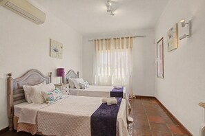 A hotel room with two beds, a window with sheer curtains, a wall-mounted air conditioner, and a small table with a lamp. - Villa Monte Galego. Private pool and garden. A space just for you. (Guia)