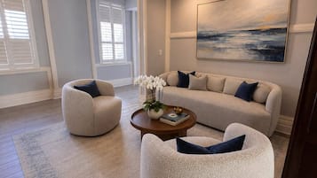 Uma sala de estar com um sofá, duas poltronas, uma mesa de centro e um quadro na parede.