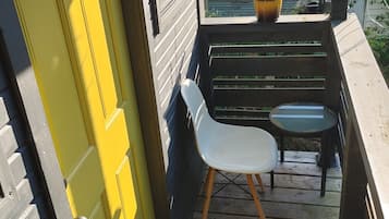Une terrasse en bois avec une porte jaune, une chaise blanche et une petite table.