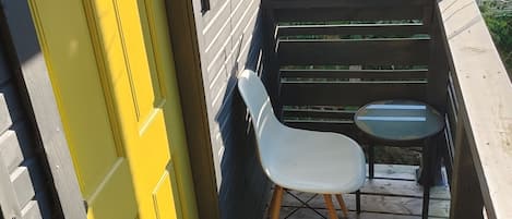 A wooden deck with a yellow door, a white chair, and a small table.