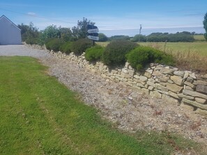 A rural landscape with a stone wall, a gravel path, and a building with a sign indicating directions to Dingle and Tralee. - Sleep4glampingtent-neartralee-countryside (Ballyduff)