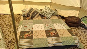 A bed with a quilted cover, pillows, and a brown bean bag in a tent-like room.