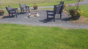 An outdoor seating area with four wooden chairs and a fire pit surrounded by gravel.