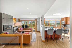 Un interior moderno con sala de estar, comedor y cocina, que incluye una chimenea, ventanas amplias y vistas al exterior.