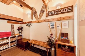Un área de recepción acogedora con un letrero que dice 'welcome', uno que dice 'thankful' y uno que dice 'saddle'. Hay cestas de mimbre, un banco de madera y un jarrón con flores.
