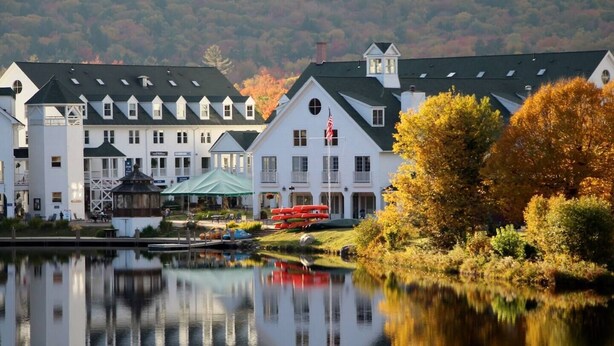 Et hotel ved søen med flere bygninger, en anløbsbro med kanoer og efterårsfarver.