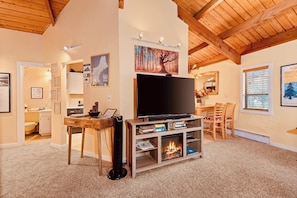 A living room with a fireplace, a television, and a dining area. - Exposed Beam Getaway - Heart of NH White Mountains (Thornton)