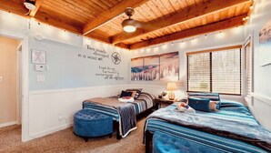 A cozy bedroom with two beds, a wooden ceiling, a wall with motivational quotes, and a window with blinds.