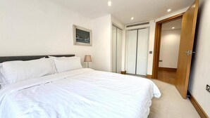 Een slaapkamer met een groot bed, een bedlampje, een ingelijst beeld aan de muur en een deur naar een kast.
