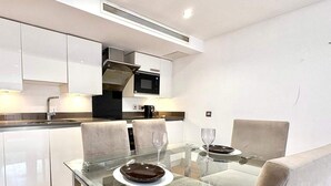 Een moderne keuken met witte kasten, een zwarte magnetron en een glazen eettafel met stoelen.