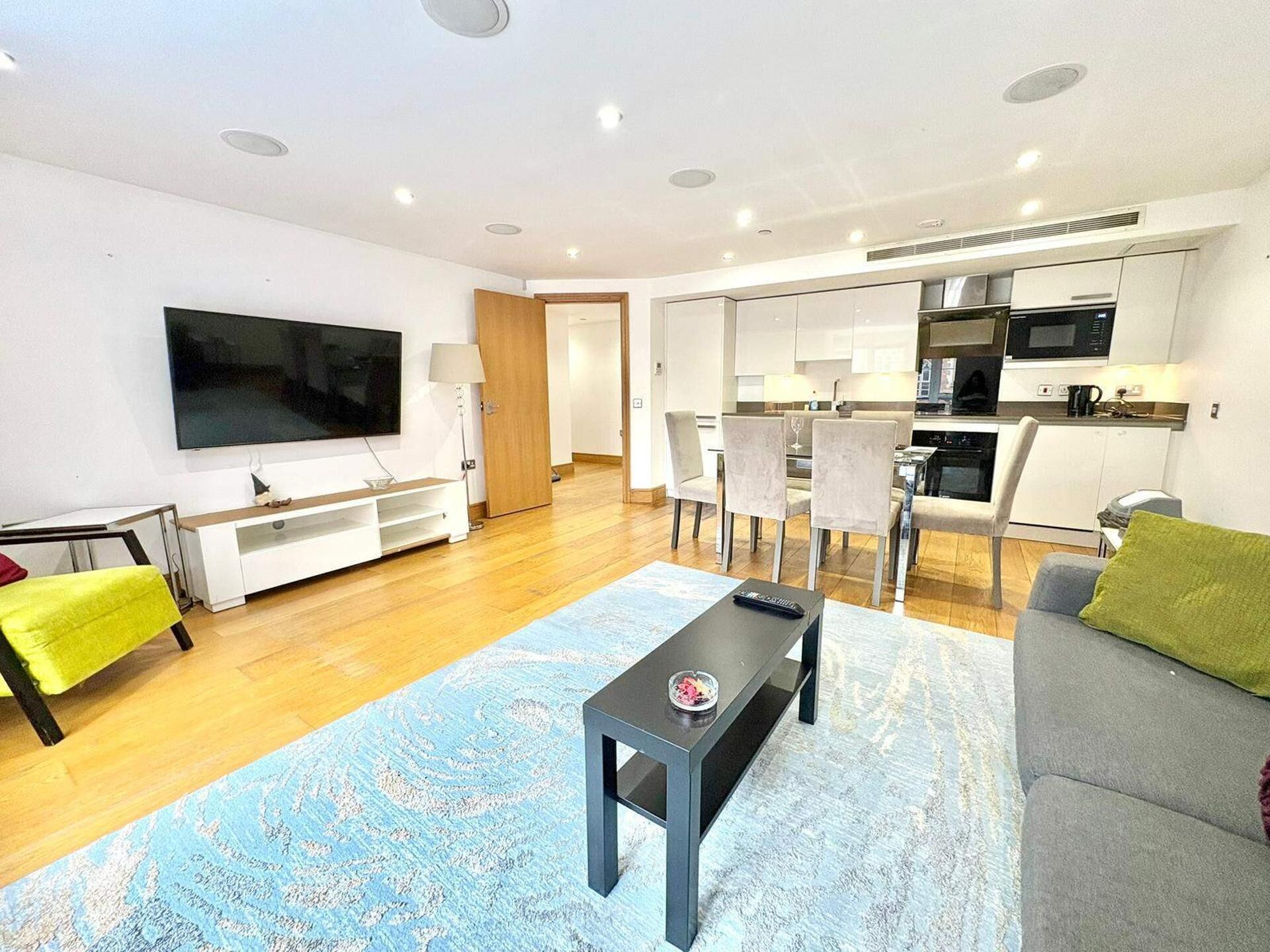 A modern living room with a flat-screen TV, a sofa, a coffee table, and a dining area with chairs.
