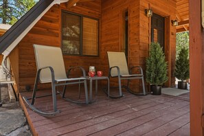 Eine Holzhütte mit Veranda, zwei Schaukelstühlen, einem kleinen Tisch mit Tassen und einem Blumentopf.