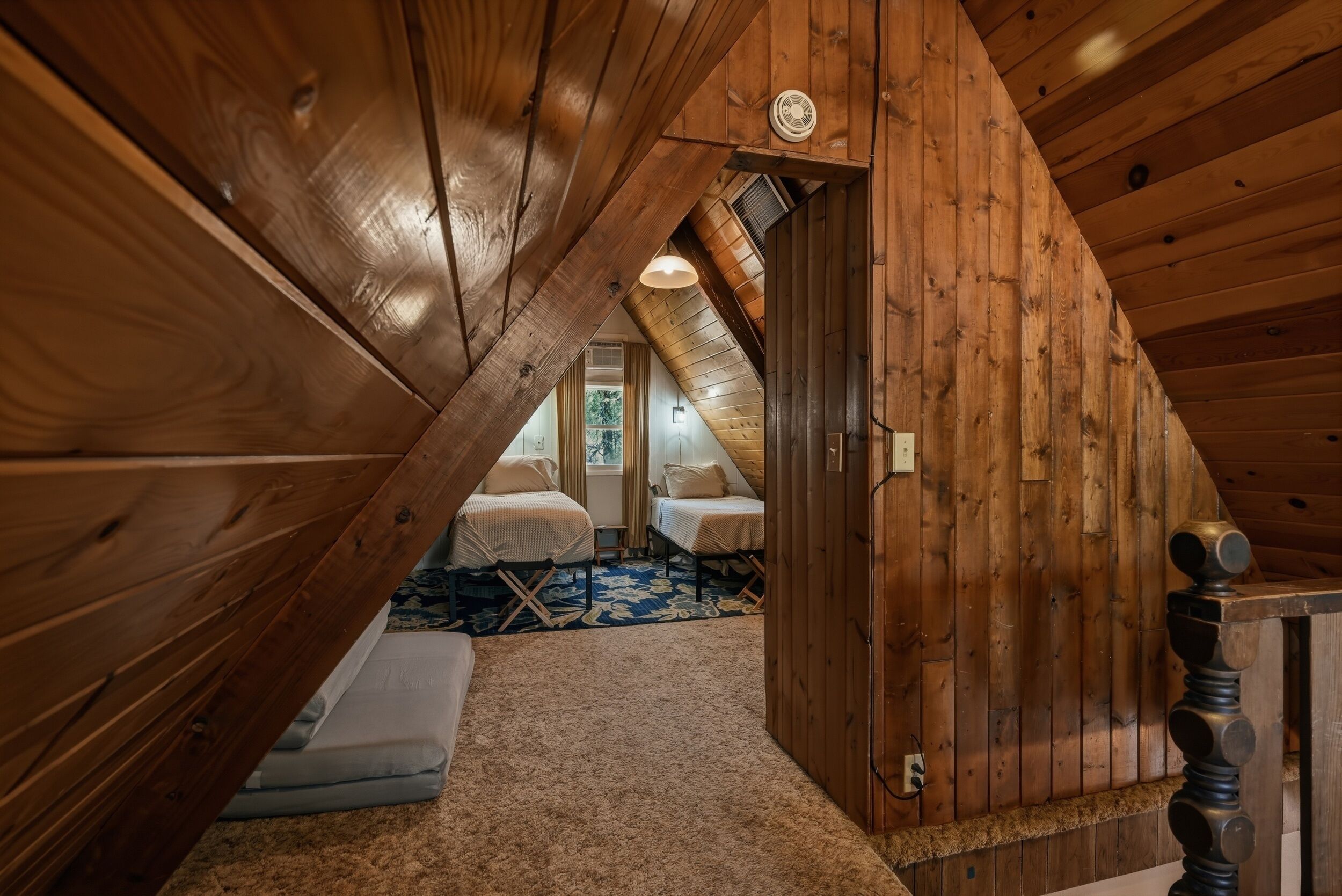 Une chambre mansardée en bois, avec un plafond en pente, un lit, une petite table et une fenêtre.