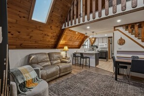 Ein Loft-Wohnraum mit Holzbalkendecke, einer Couch, einem Essbereich und einer Küche.