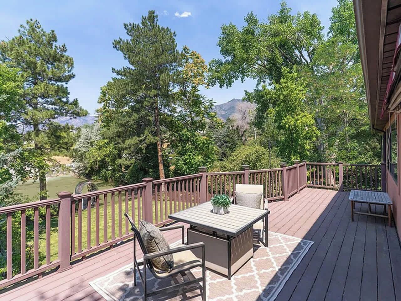A deck with a table and chairs, surrounded by a wooden railing, overlooking a natural landscape.