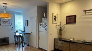 A compact kitchen with a refrigerator, microwave, and a dining area with a table and chairs. - Charming Shared Unit with Host. Beautiful Park Slope on 5th Ave (Brooklyn)