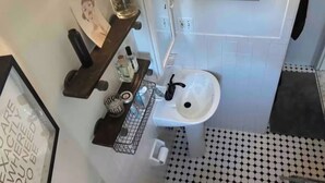 A bathroom with a white sink, a mirror, a framed picture on the wall, and a black and white patterned floor. - Charming Shared Unit with Host. Beautiful Park Slope on 5th Ave (Brooklyn)