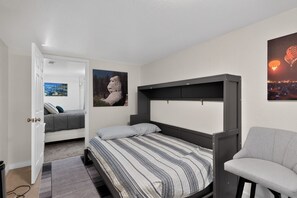 A bedroom with a bed, a chair, and a door leading to another room. - Midtown Reno Apartment | Workspace Near UNR (Reno)