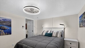 Et soveværelse med seng, natborde, ventilator i loftet og billedkunst på væggen.