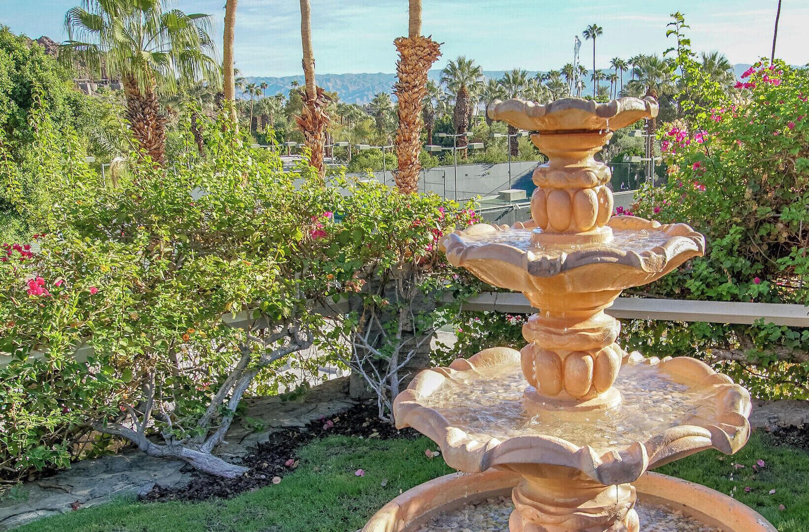 Uma fonte de pedra escalonada com água, rodeada por vegetação exuberante e plantas floridas.