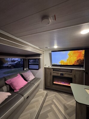 A modern RV interior with a flat-screen TV, a fireplace, and a seating area.