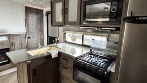 Une cuisine de taille réduite, équipée d’une cuisinière, d’un four à micro-ondes et d’un réfrigérateur, avec des meubles de rangement en bois et une fenêtre.