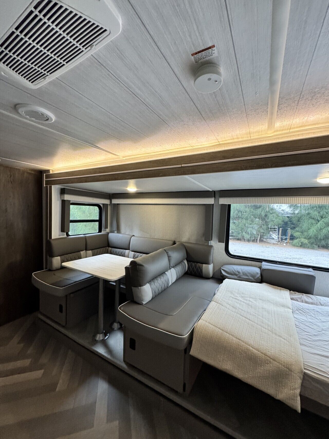 A modern RV interior with a sectional sofa, a dining table, and a window providing a view of the outdoors.