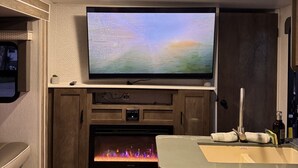 Un intérieur de camping-car moderne, doté d’un téléviseur à écran plat fixé au-dessus d’une cheminée, de meubles en bois et d’un coin cuisine.