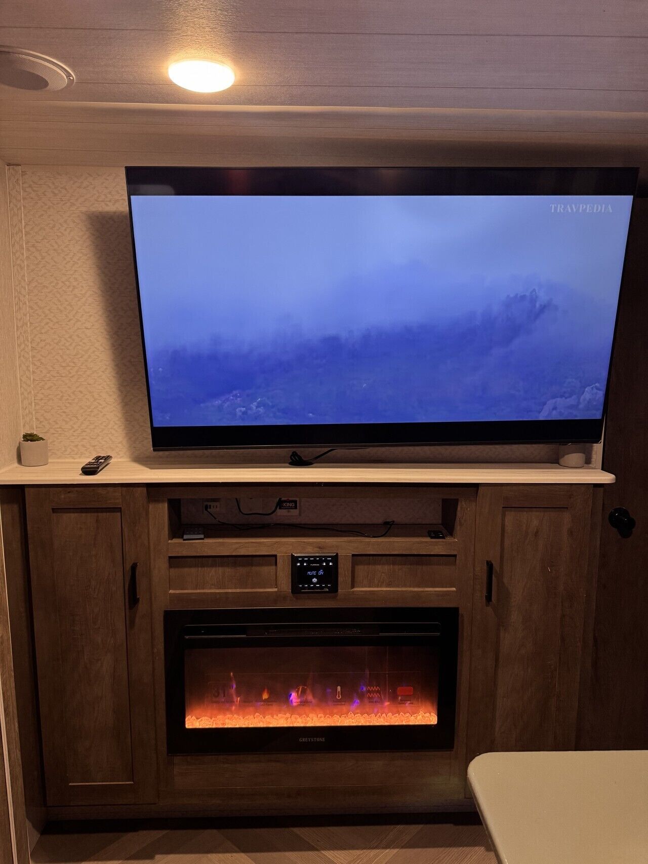 A television mounted on a wooden cabinet above a fireplace with a remote control on the cabinet.